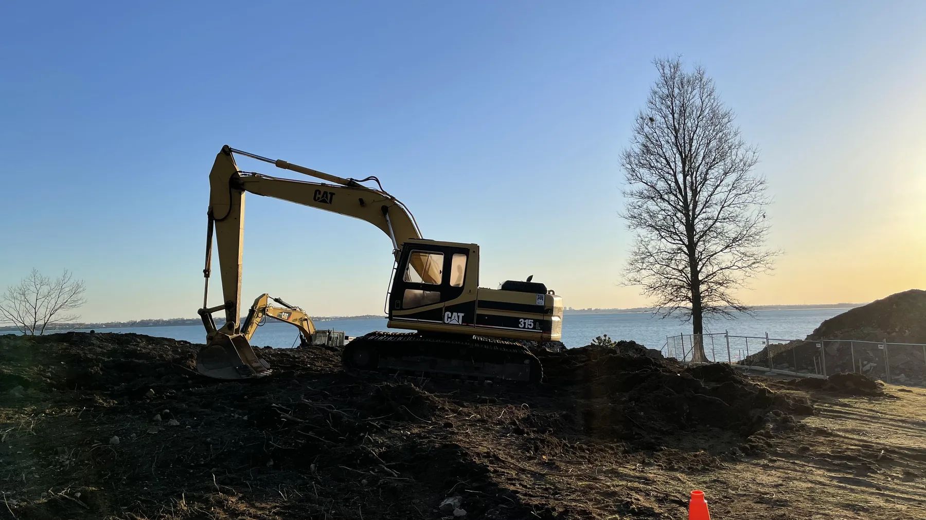Excavator clearing a waterfront site at sunrise